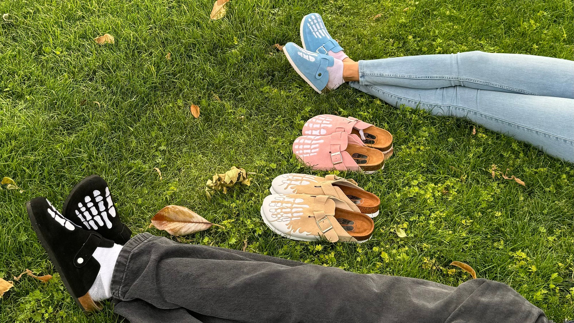 Two pairs of shoes on grass with a person lying down wearing black pants and a backpack.